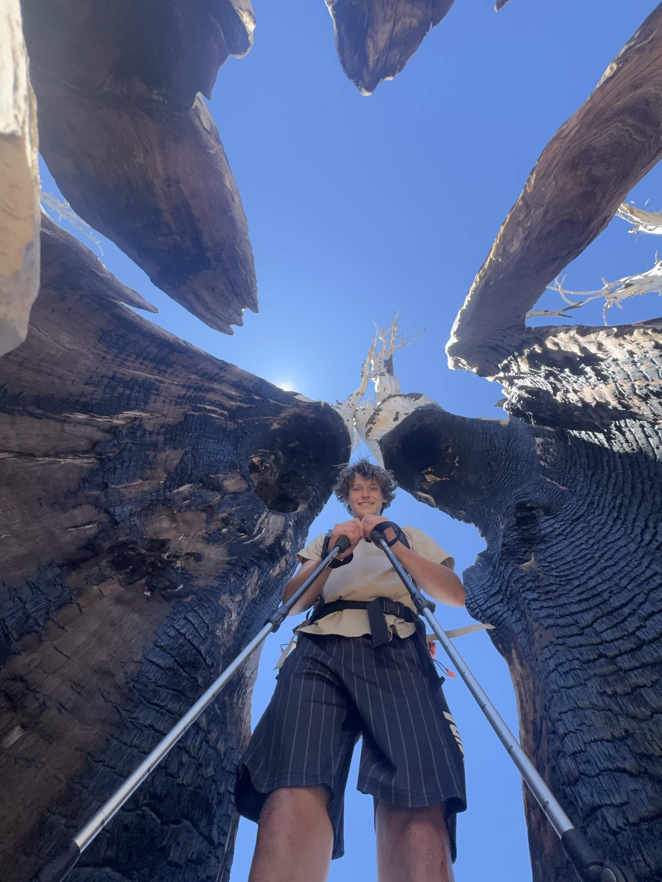 A hiker stands on rock beneath a narrow opening between canyon walls, photographed from below.
