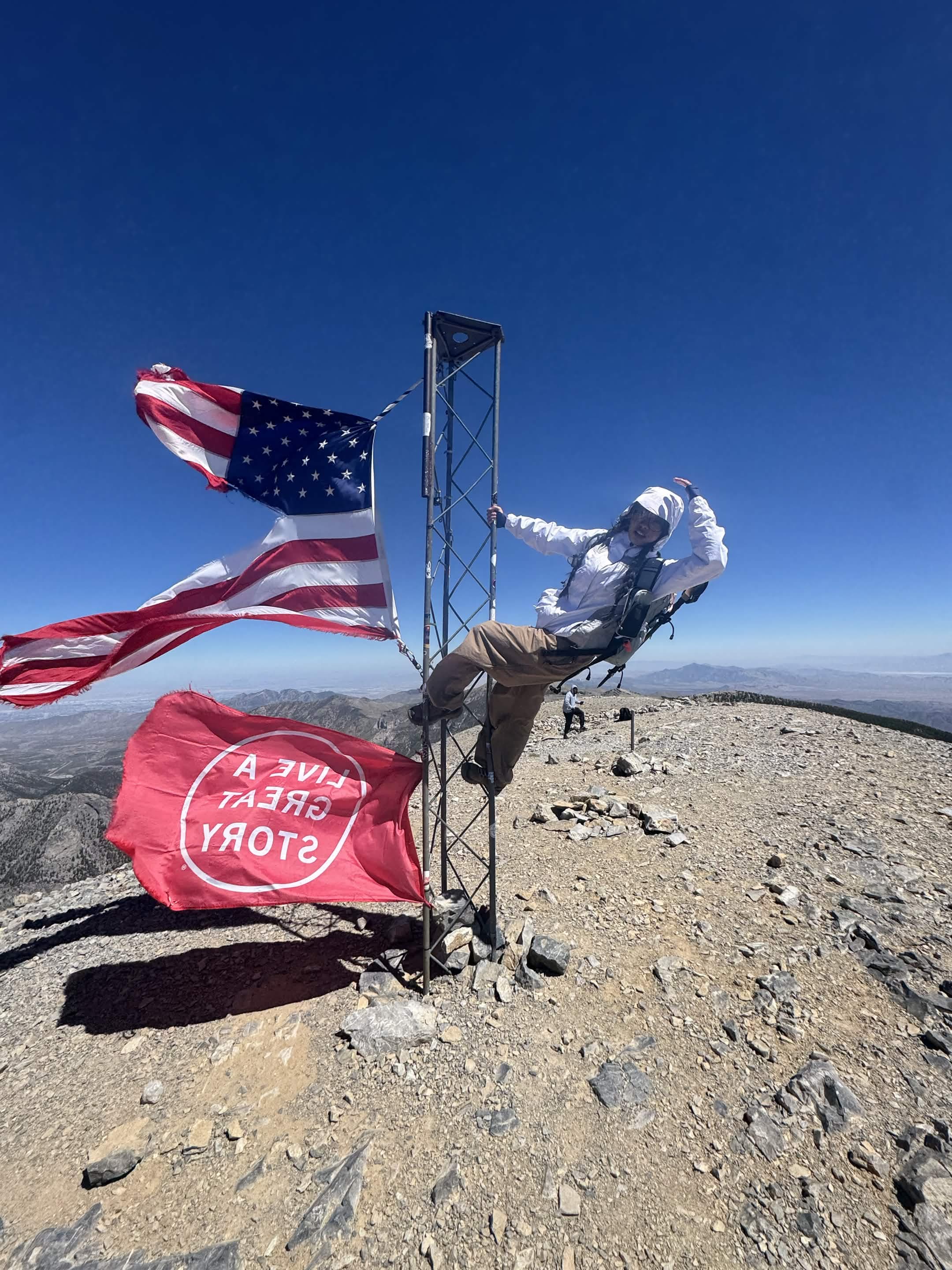 An American flag and summit marker stand on a rocky peak under a deep blue sky.