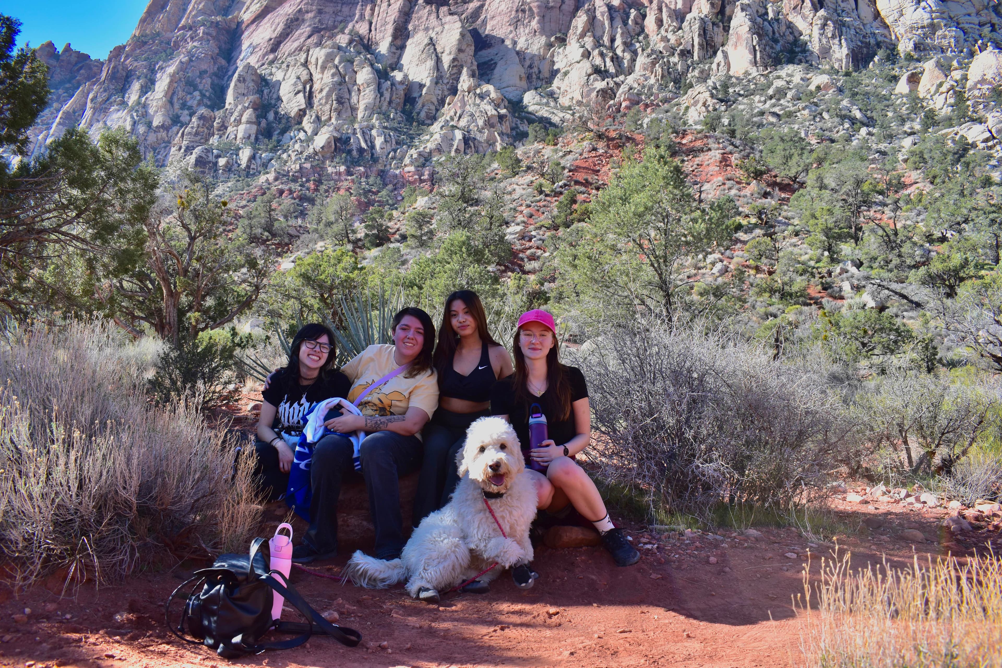 Club members and Mochi sit together beside a red-rock canyon trail.